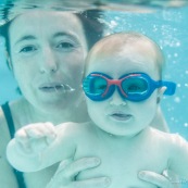 Portrait de bebe sous l'eau. Sa maman a proximite. Bebe avec des lunettes sous l'eau dans une piscine. En train d'apprendre a nager.