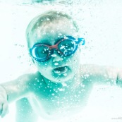 Portrait de bebe sous l'eau. Sa maman a proximite. Bebe avec des lunettes sous l'eau dans une piscine. En train d'apprendre a nager.