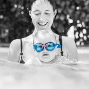 Bebe dans une piscine avec sa maman. En train d'apprendre a nager. Avec des lunettes de piscine.