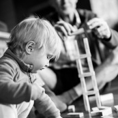 bebe enfant petite fille en train de jouer avec son grand-pere en arriere plan. Joue avec un jeu en bois (jouet).